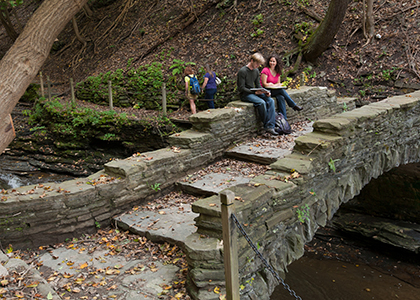 two student sitting on a stone bridge over a creek