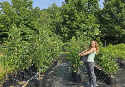 Student holding a potted tree outside