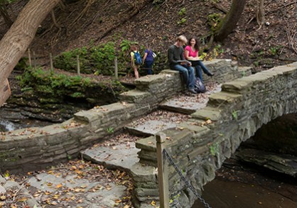 two student sitting on a stone bridge over a creek