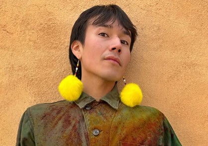 Image of person with short black hair and yellow pom pom earrings