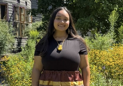 Young woman with long brown hair and a brown shirt and colorful long skirt