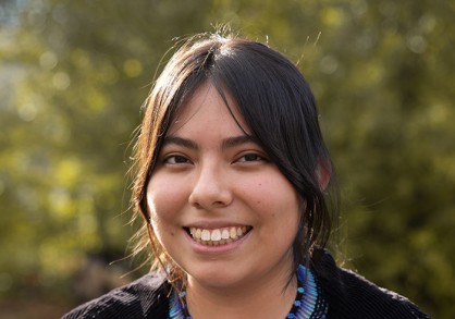 young woman with dark brown hair and a white shirt with a black sweater