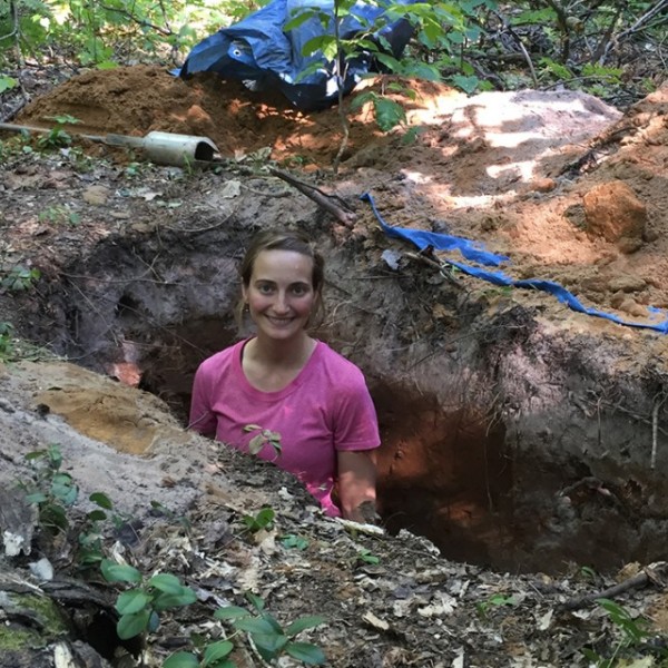 Researcher stands in a soil pit in the forest