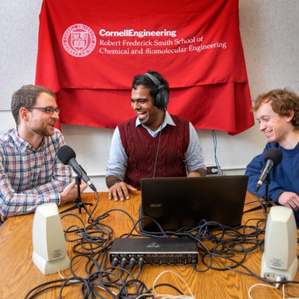 Students sit with podcast equipment in front of a Cornell Engineering flag
