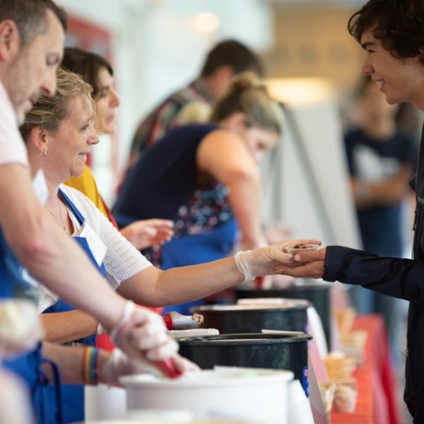 Workers scoop and hand ice cream to students