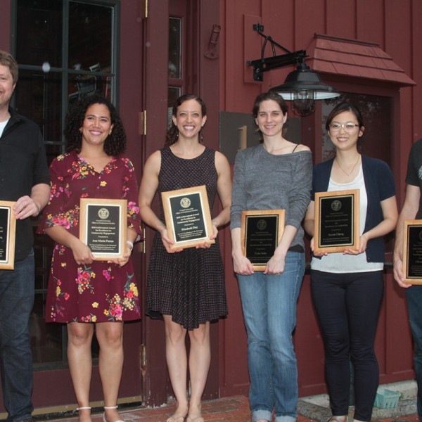 Six postdocs stand in a row holding plaques