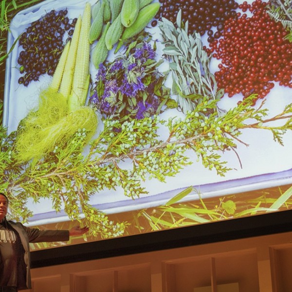 Sean Sherman stands in front of a presentation screen with food presented on it
