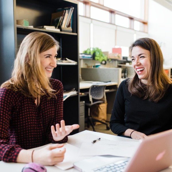 Two women laugh while sitting at a table
