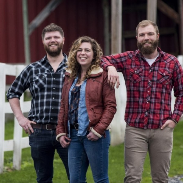 two young men and young woman stand outside of a barn