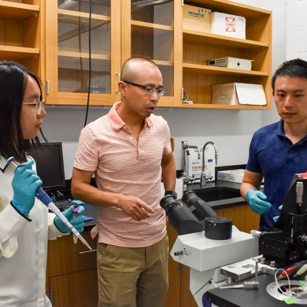 One female and two male researchers standing around a microscope and talking