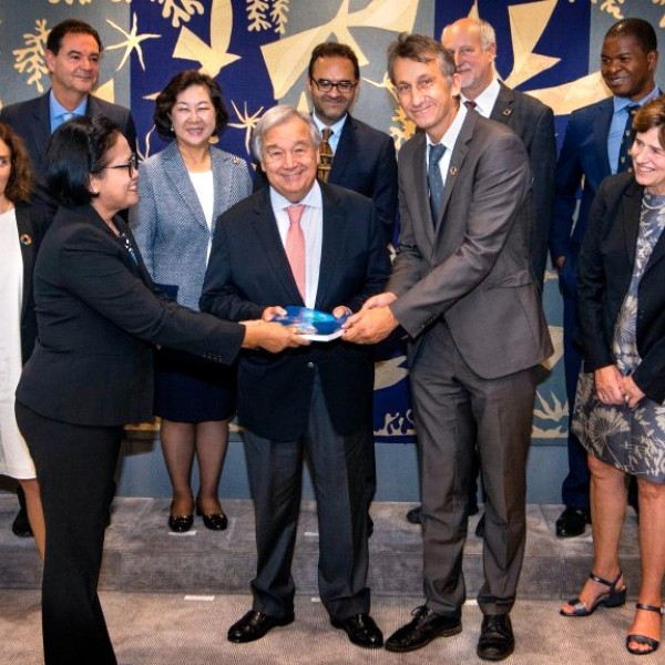 A large group of men and women smiling at the camera. One woman and two men in the middle all handing each other a book.