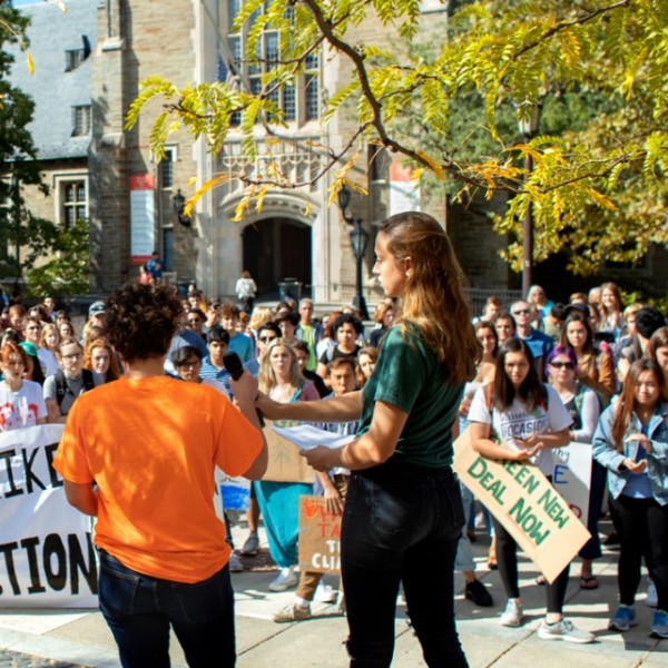Two female students standing before and speaking to a large crowd outside on Cornell's campus