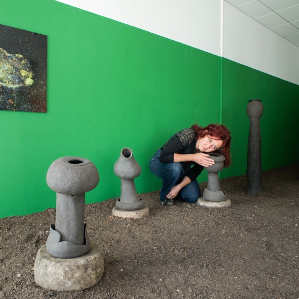 A red-headed woman crouching down with her ear over a tall grey structure