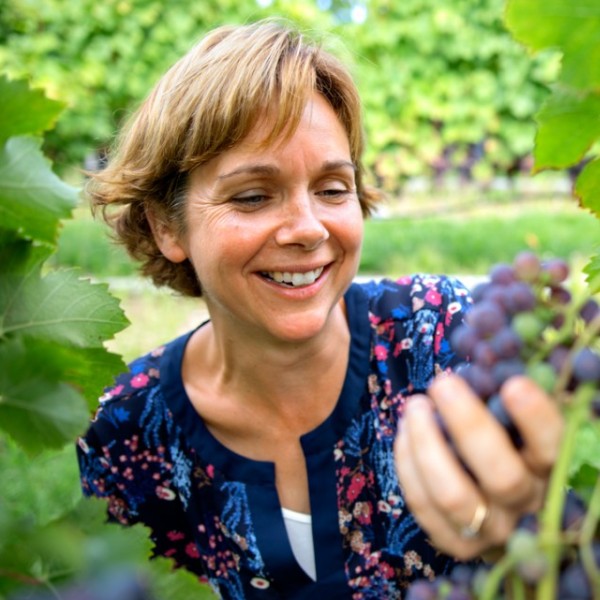 A woman with short brown hair smiling and looking at grapes hanging from a vine