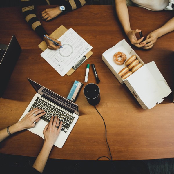 An arial view of men and women sitting at a table with laptops, paper and donuts, collaborating