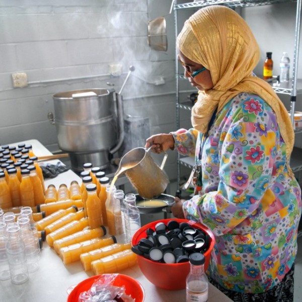 A woman standing in a kitchen pouring sauce into bottles