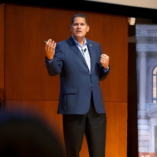 A man in a navy suit standing and talking on a stage in front of a Dyson banner