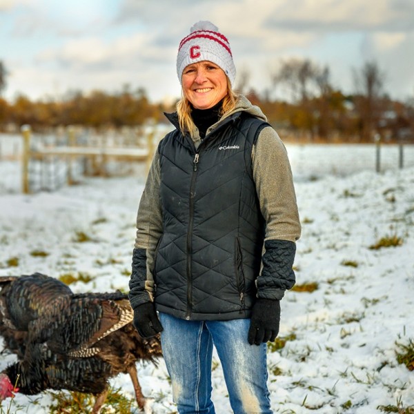 A woman standing outside in a snow-covered field with turkeys behind her
