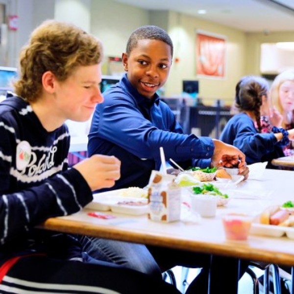 Five middle schoolers sit at a cafeteria table eating lunch and cracking jokes