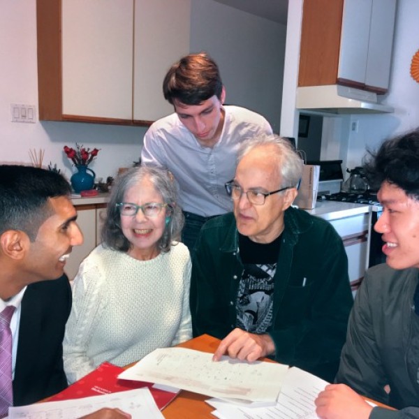 Three young men talk with an older couple around their kitchen table.