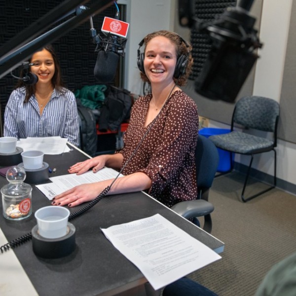 Two women and one male sitting at a table in front of microphones talking and laughing with one another