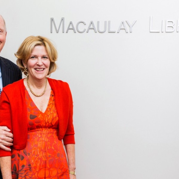 A man and woman standing in front of a white wall with a sign that says Macaulay Library