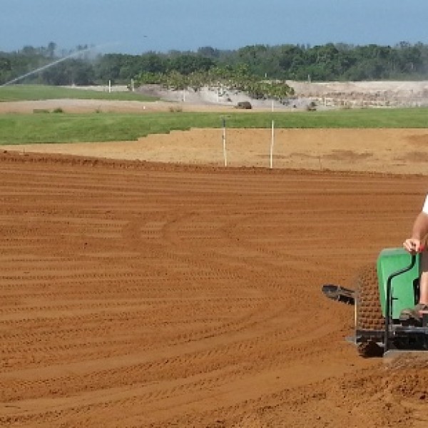 A man wearing a hat uses a piece of John Deer farm equipment in an open field