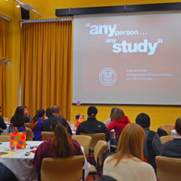 Many people sit in a room and listen to a woman speak at a podium and give a presentation
