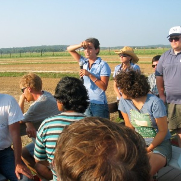 A group of people stand outside listening to a woman speak into a microphone