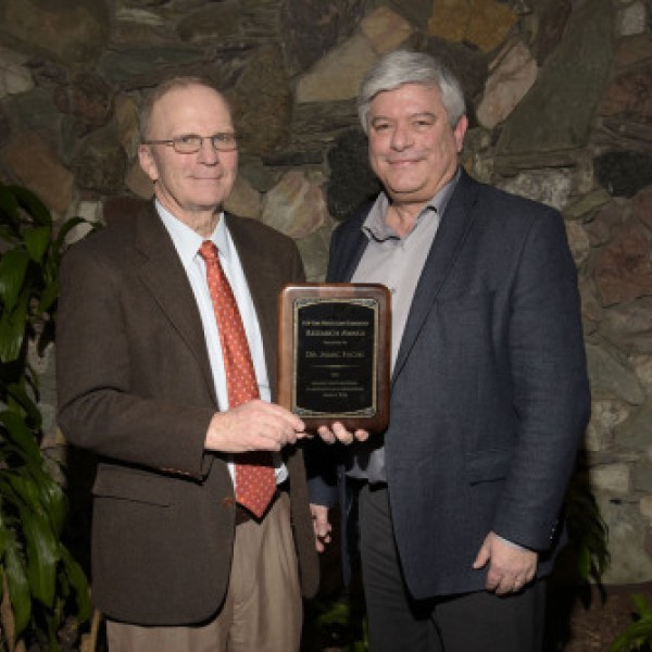 Two men stand together holding an award
