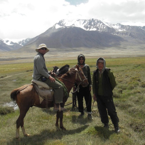 One man sits on horseback while two men stand besides him in the Pamir Mountains of Afghanistan