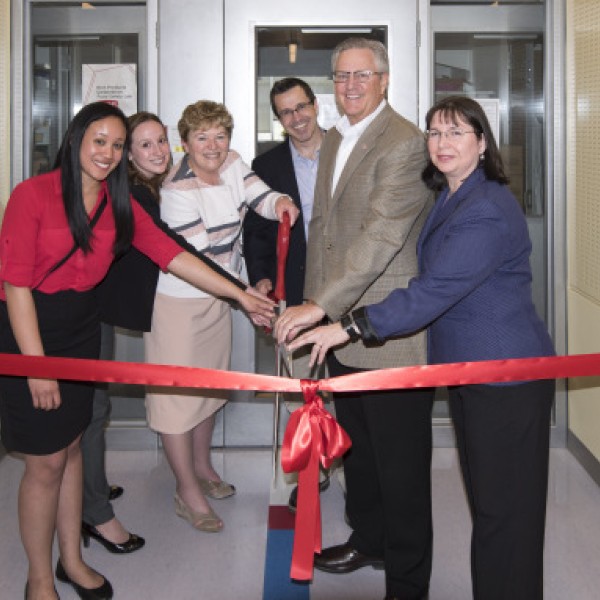 A group of people cut a red ribbon in front of a new facility for food safety research