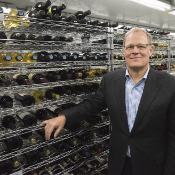 A man stands in front of shelves containing bottles of wine