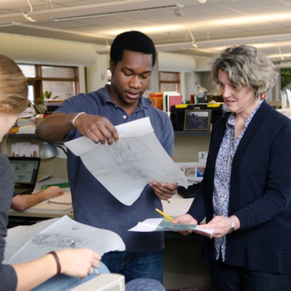 Three people hold and look at papers inside a studio