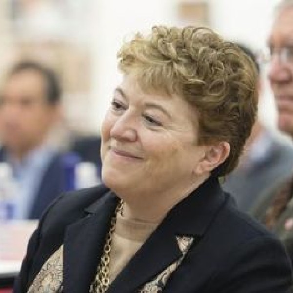 A woman in focus sits in front of a crowd of people who are blurred in the background