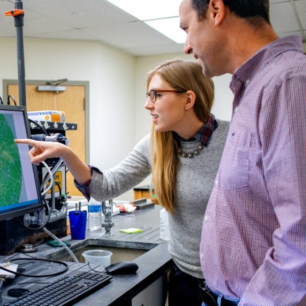 A man and woman stand at a computer gesturing toward it