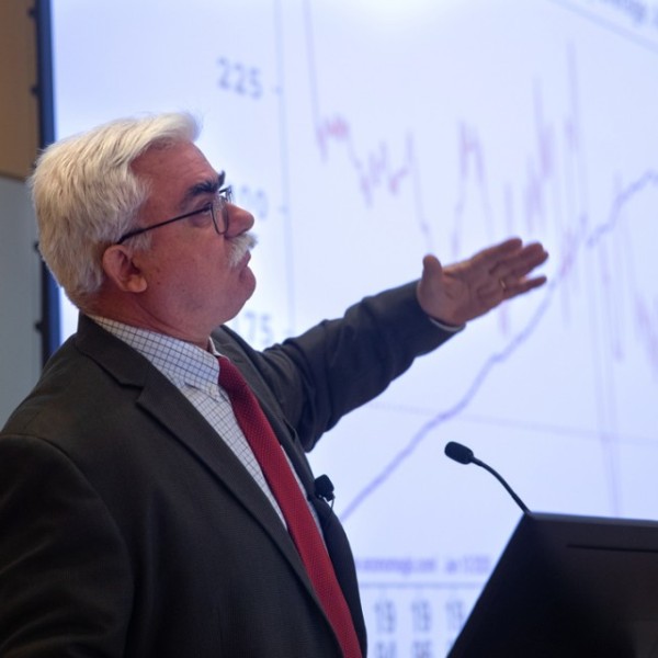 A man standing and talking at a podium in front of a large screen