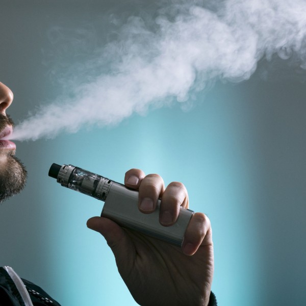 The silhouette of a man vaping in front of a blue background