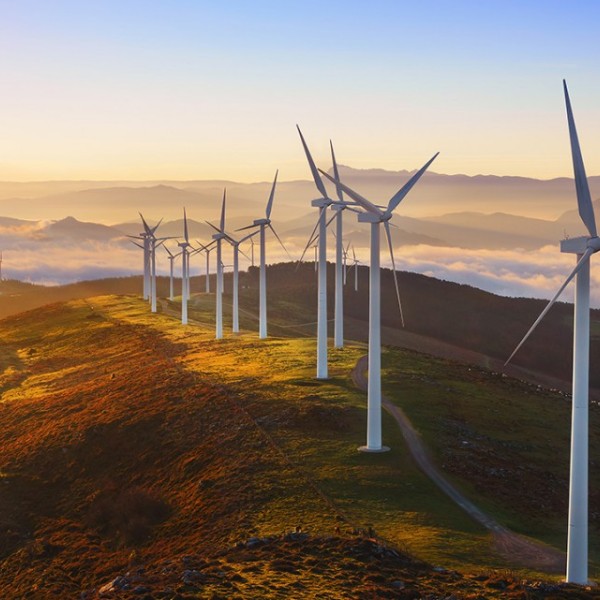 Tall white wind turbines on top of a mountain at sunset