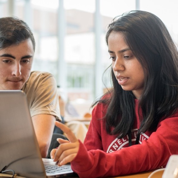A male and female student sit at a table and talk about something on a laptop