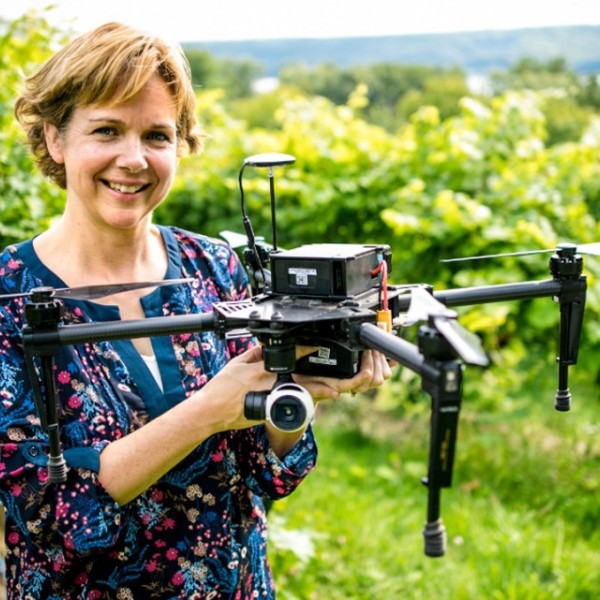 Woman stands with drone in middle of vineyard