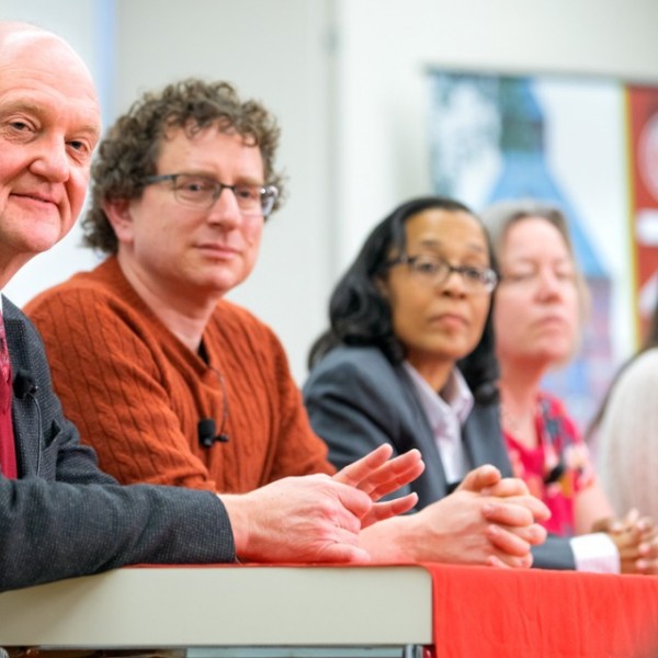 Two men and three women sitting at a table in front of microphones