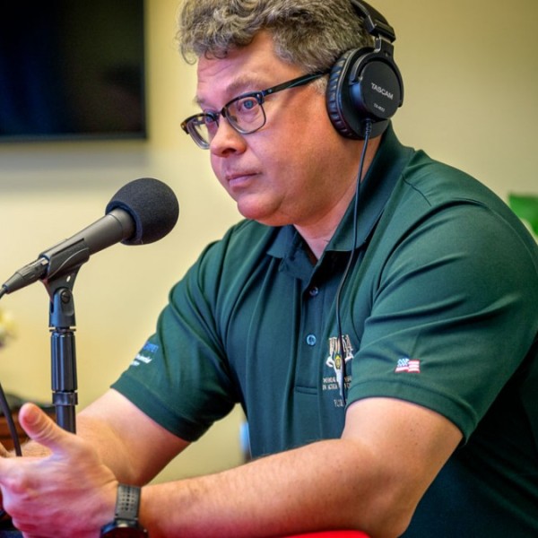 A man sitting at a table wearing head phones and talking into a microphone