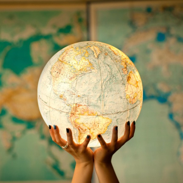 Two hands hold a globe in front of a map of the world