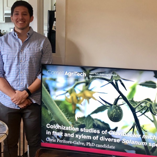 Man stands proudly next to TV showing his dissertation