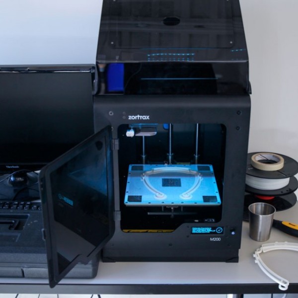 A computer and a 3D printing machine sit on a desk as a horseshoe is printed