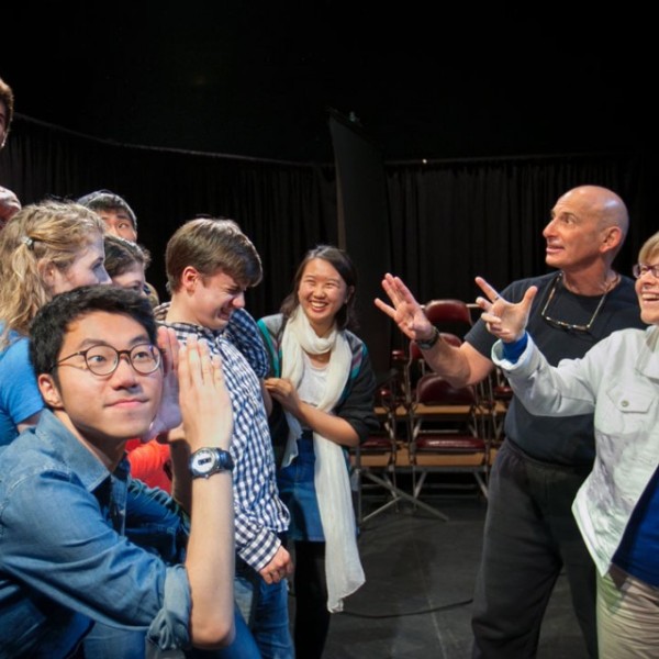 A group of people all act colorfully as two people gesture towards them