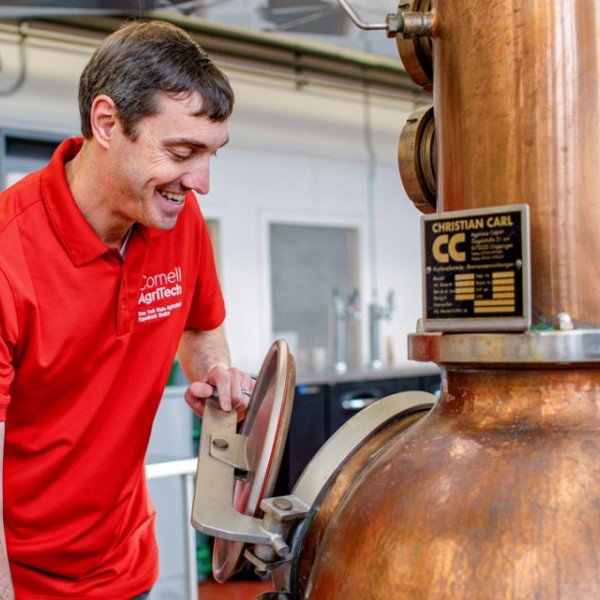 Smiling man stands next to a metal distillation device