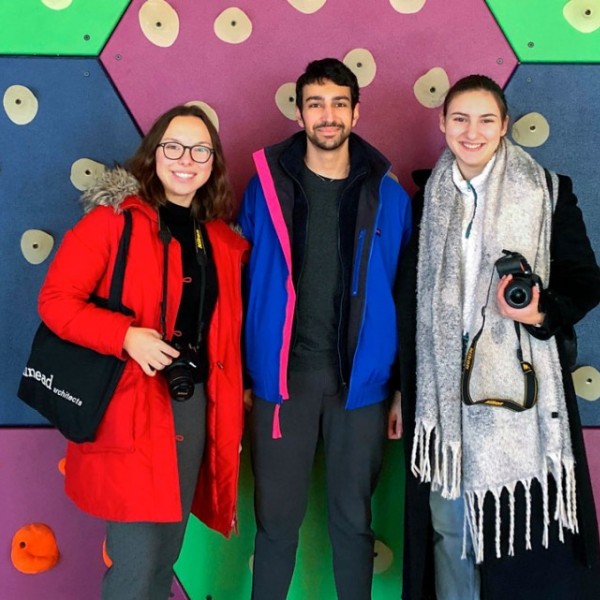 A man and two females standing together with a colorful wall behind them