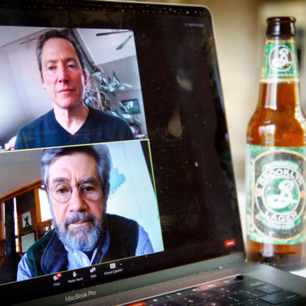 A computer laptop screen shows two men discussing beer.